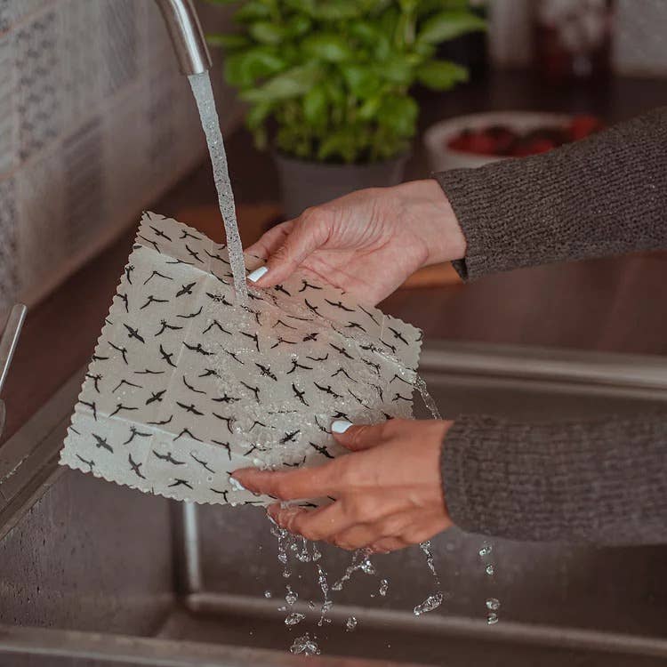 Person washing a patterned dishcloth under running water in a kitchen sink.