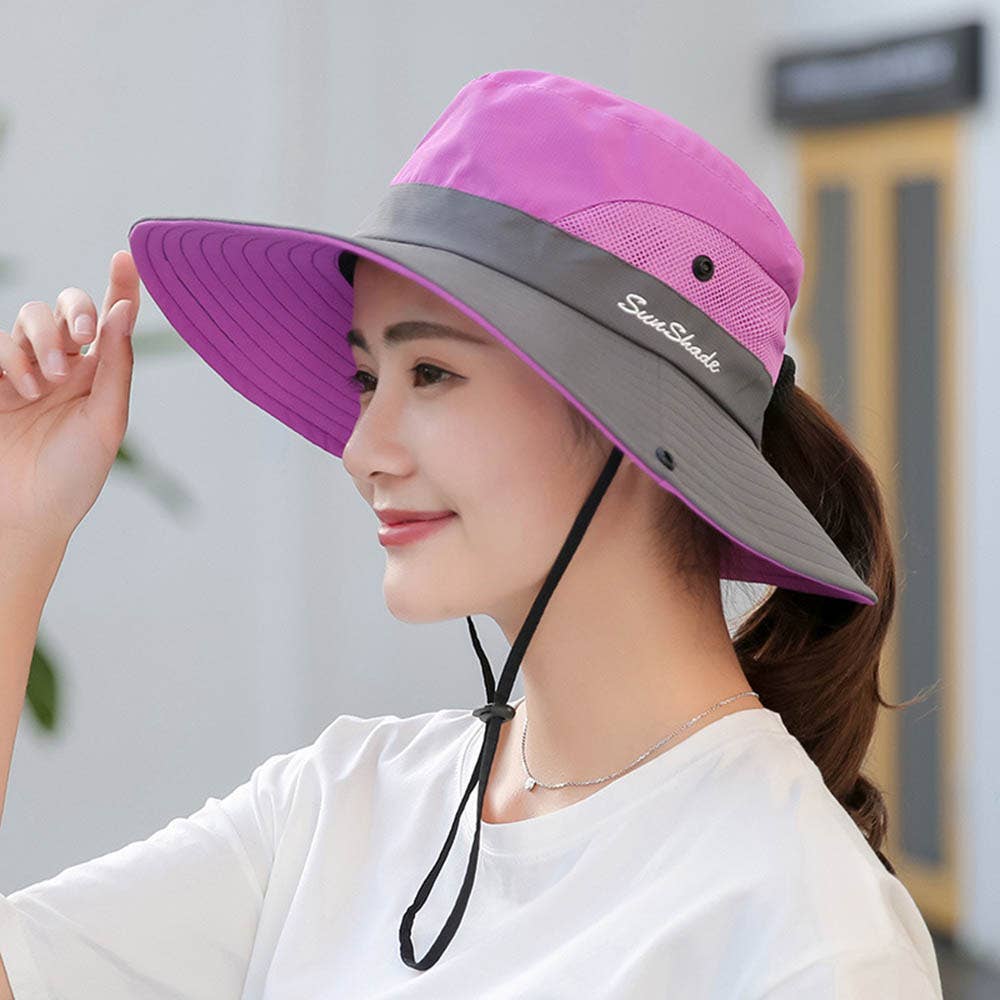 Woman wearing a purple and gray wide-brimmed hat with a brand logo, outdoors.