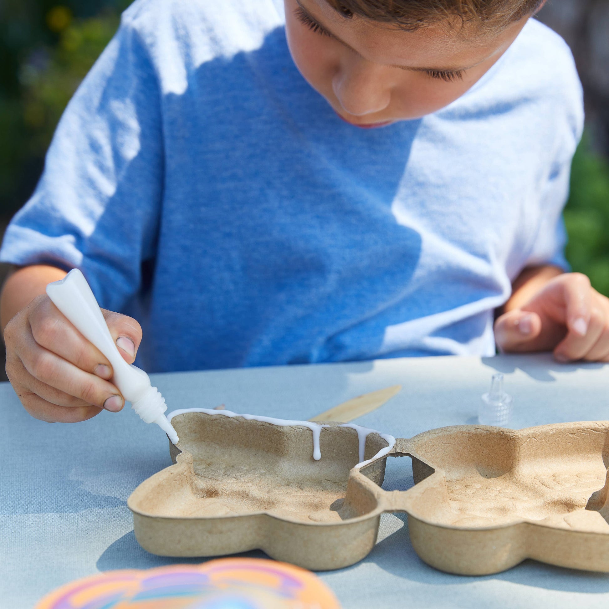 Child gluing butterfly wings made from cardboard boxes outdoors