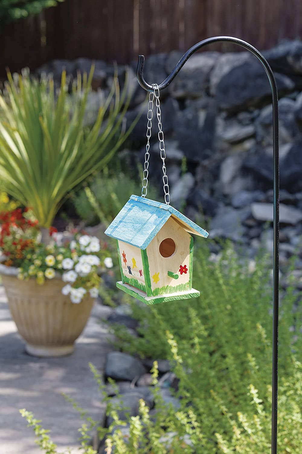 Decorative birdhouse hanging in a garden with plants and rocks in the background