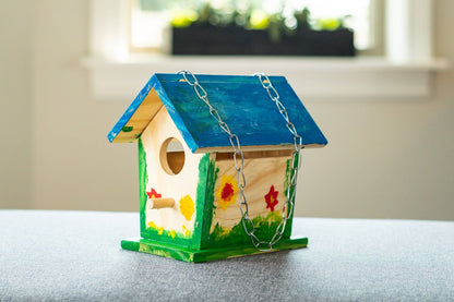 Colorful wooden birdhouse with a blue roof on a gray surface.