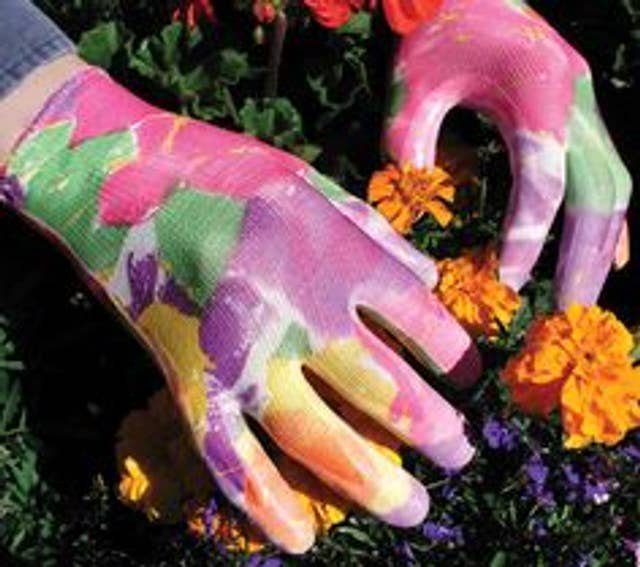 Colorful gardening gloves with floral pattern on a background of flowers and greenery