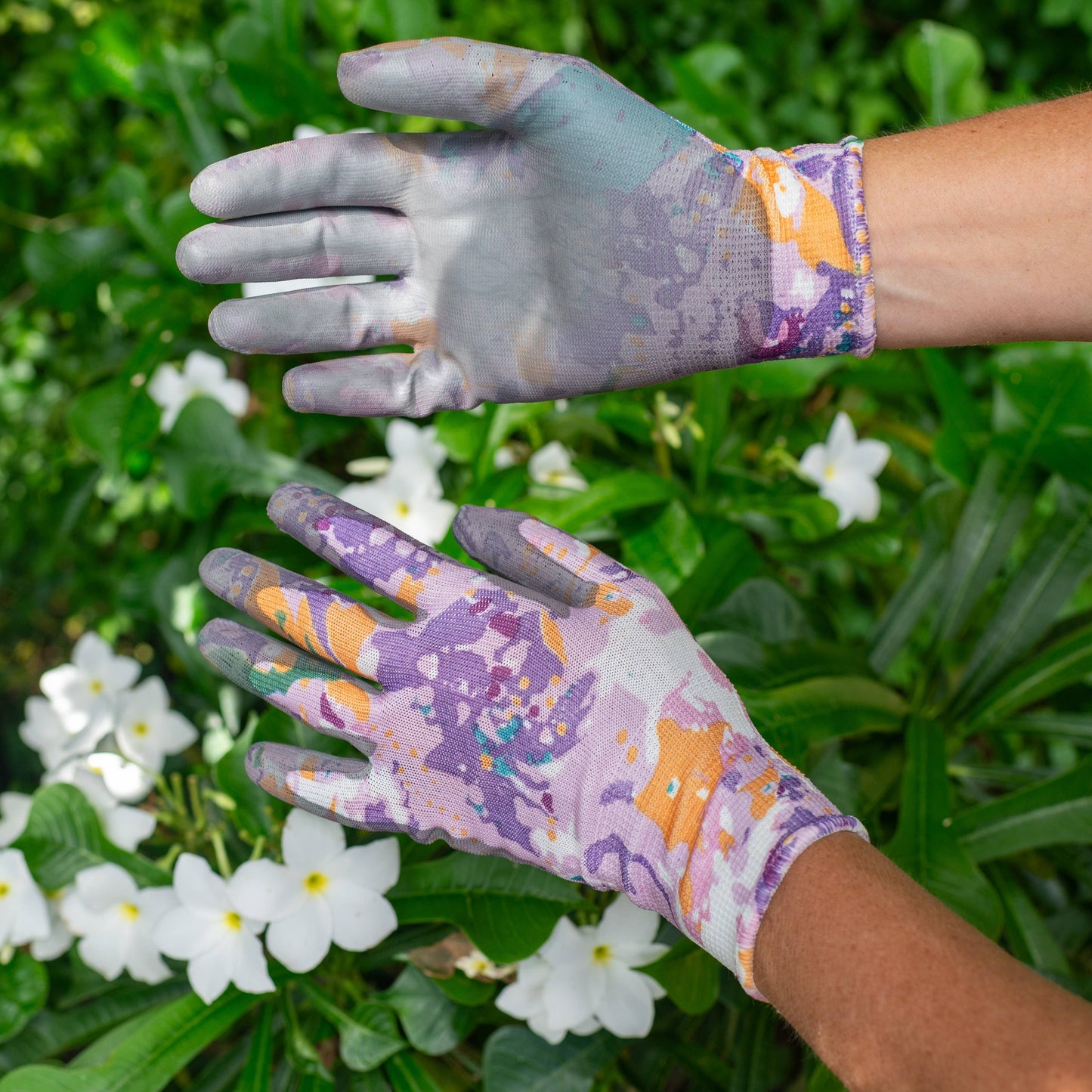 Gardening gloves with floral pattern worn by a person against a green plant and white flowers background