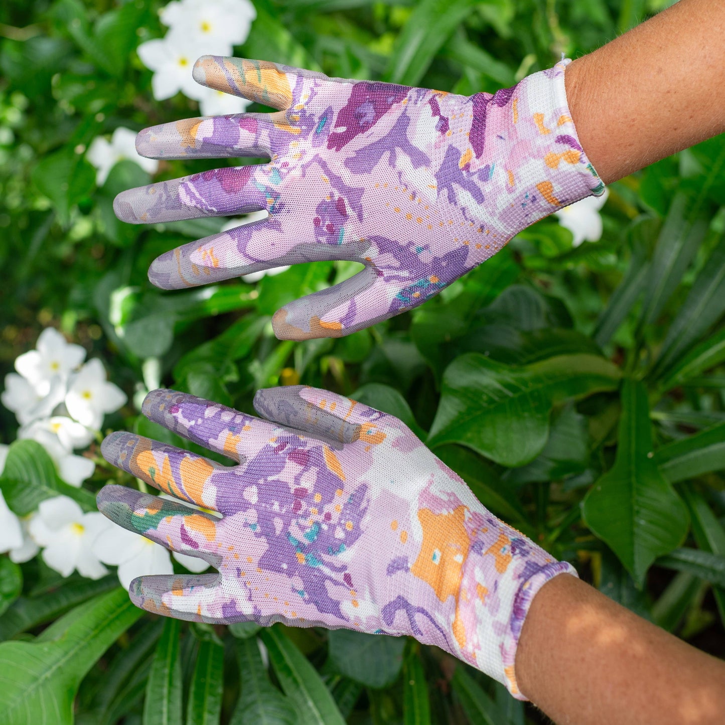 Pair of gardening gloves with a colorful pattern worn by a person against a green leafy background.