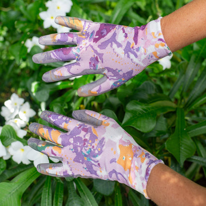 Pair of gardening gloves with a colorful pattern worn by a person against a green leafy background.
