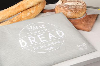 Gray bread bag with 'Fresh Baked Bread' text, placed on a table with bread and a knife.