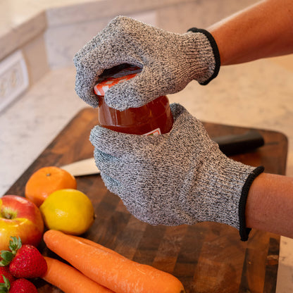 Person wearing cut-resistant gloves holding a jar on a kitchen counter with fruits and vegetables.