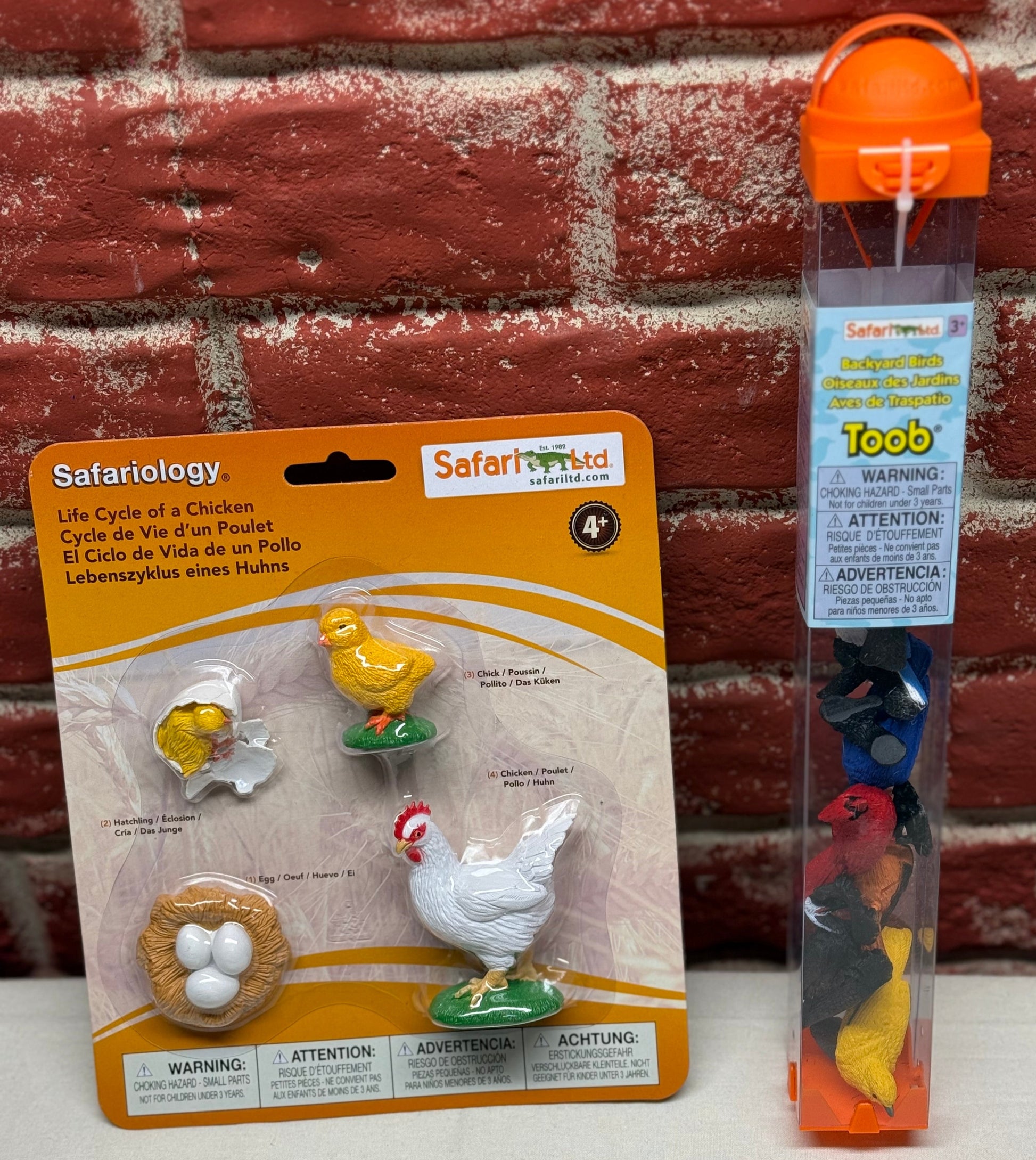 Safariology toy set packaging and Toob with colorful animals against a brick wall.