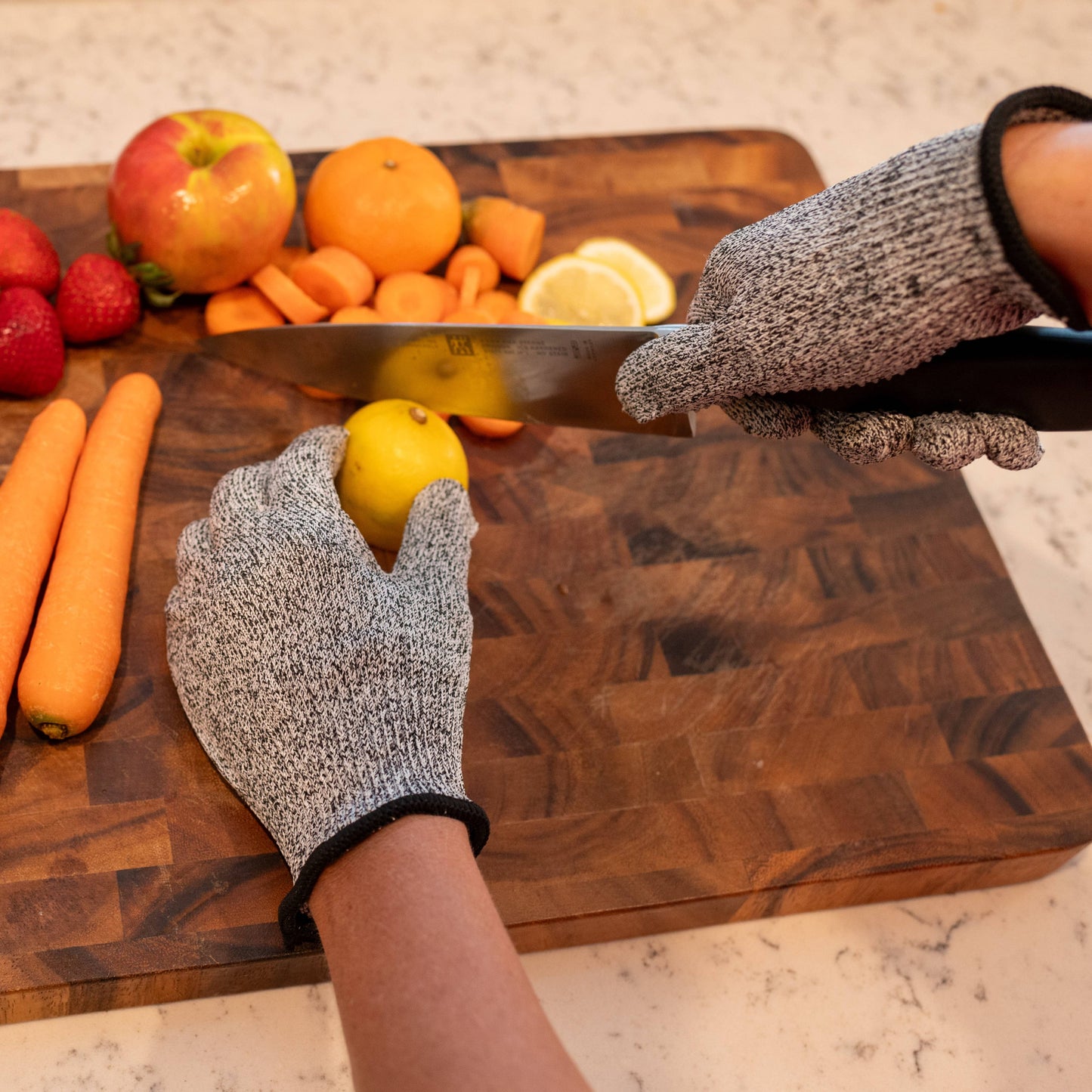 Person cutting a lemon on a wooden cutting board with various fruits and vegetables around.