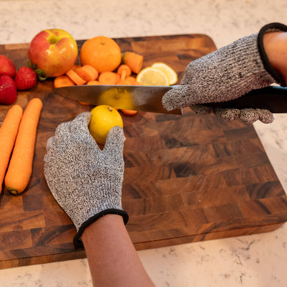 Person cutting a lemon on a wooden cutting board with various fruits and vegetables around.