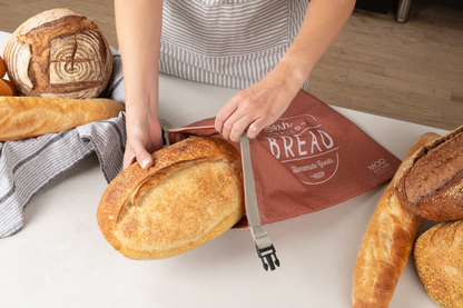 Person holding a loaf of bread with a 'Bread' bag in the background
