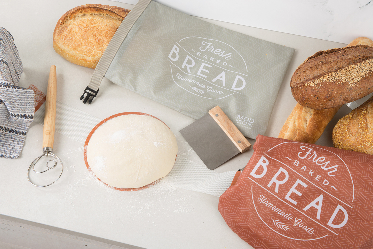 Bread bags with 'Fresh Baked' text, loaves of bread, and baking tools on a white surface.