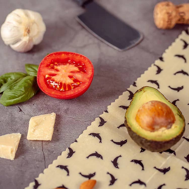 Half-cut avocado on a plate with basil, tomato, garlic, and cheese on a gray surface.