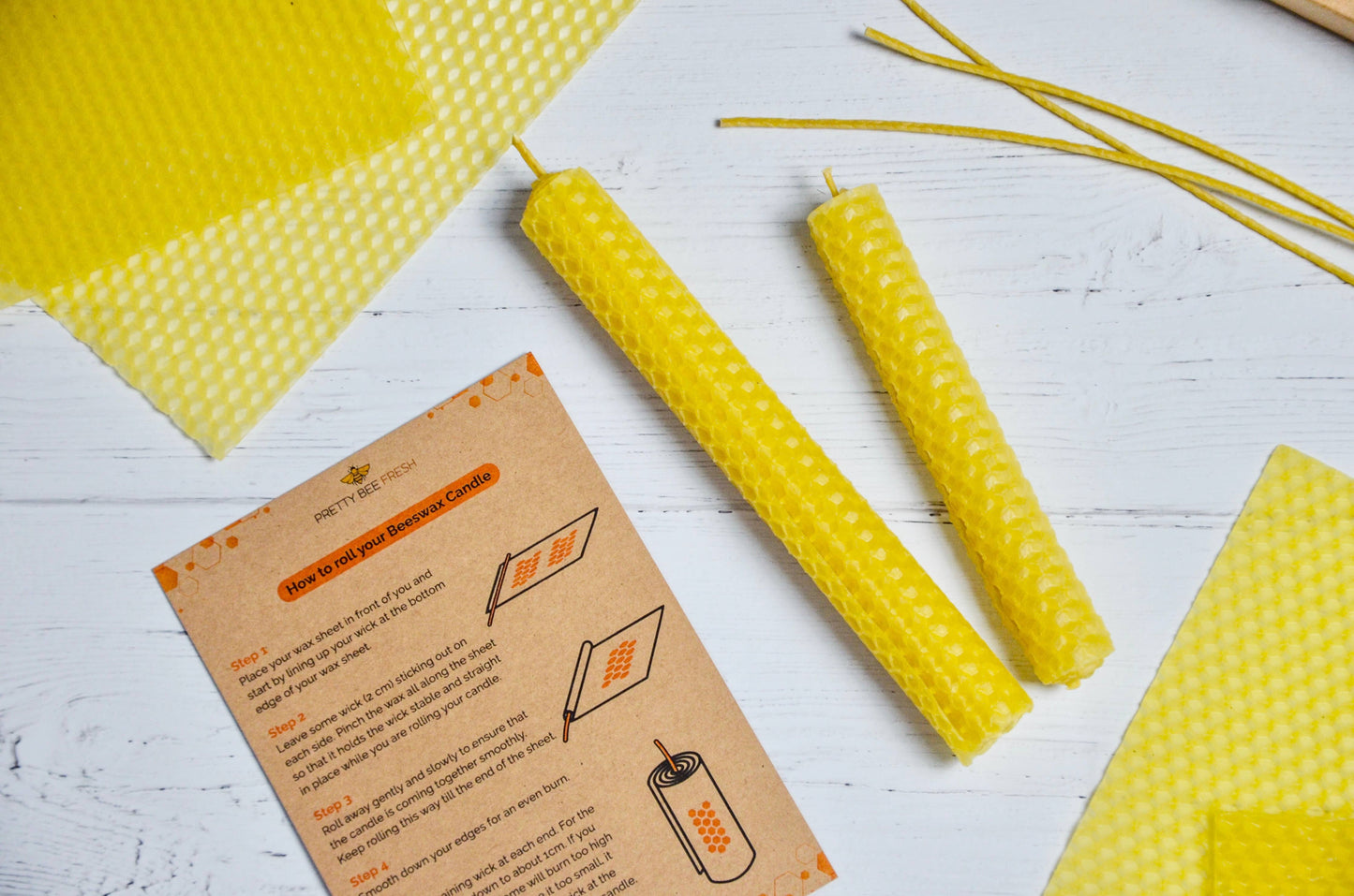 Yellow beehive candles and a card on a white wooden surface